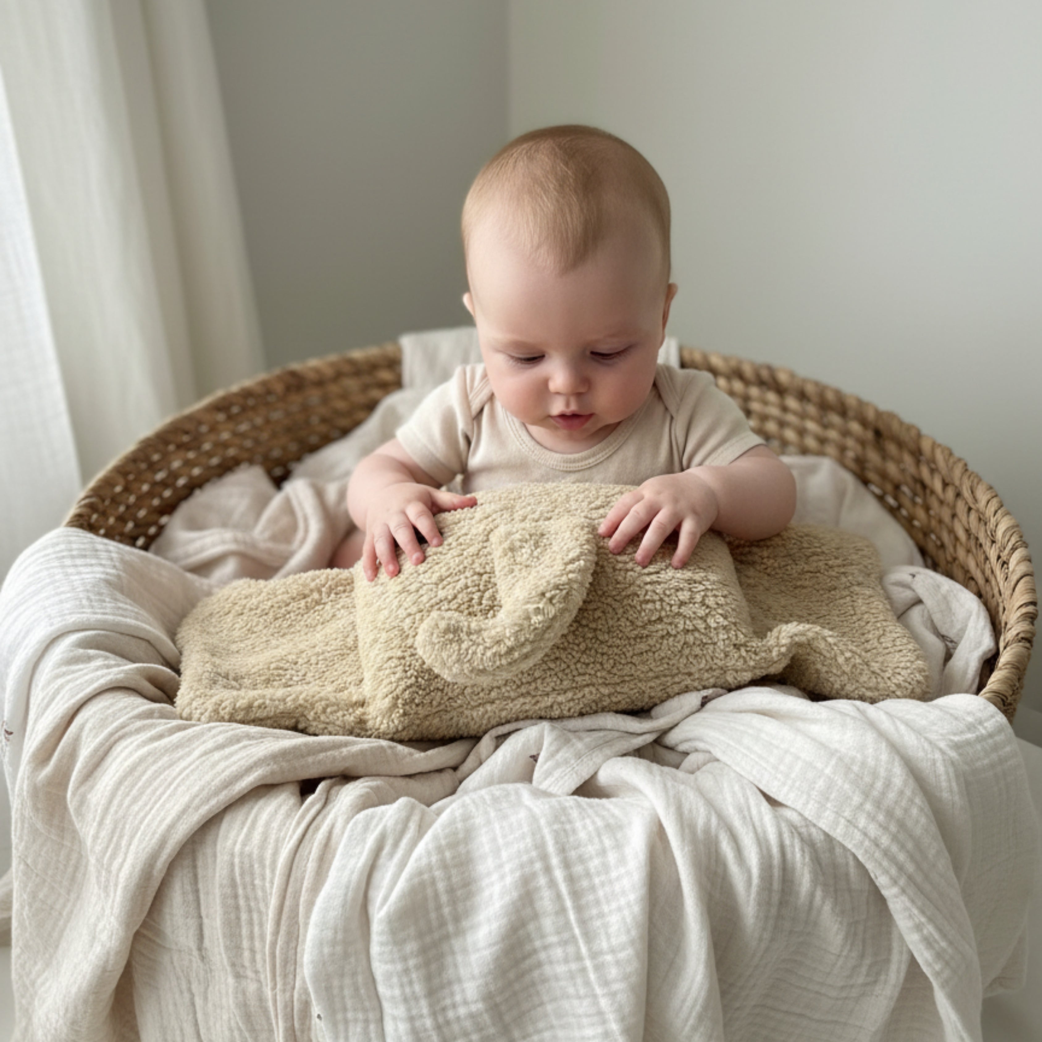 A baby in a woven basket touching Ellie the Elephant Sleep Companion — a handmade plush elephant designed for calm sensory discovery and early comfort.