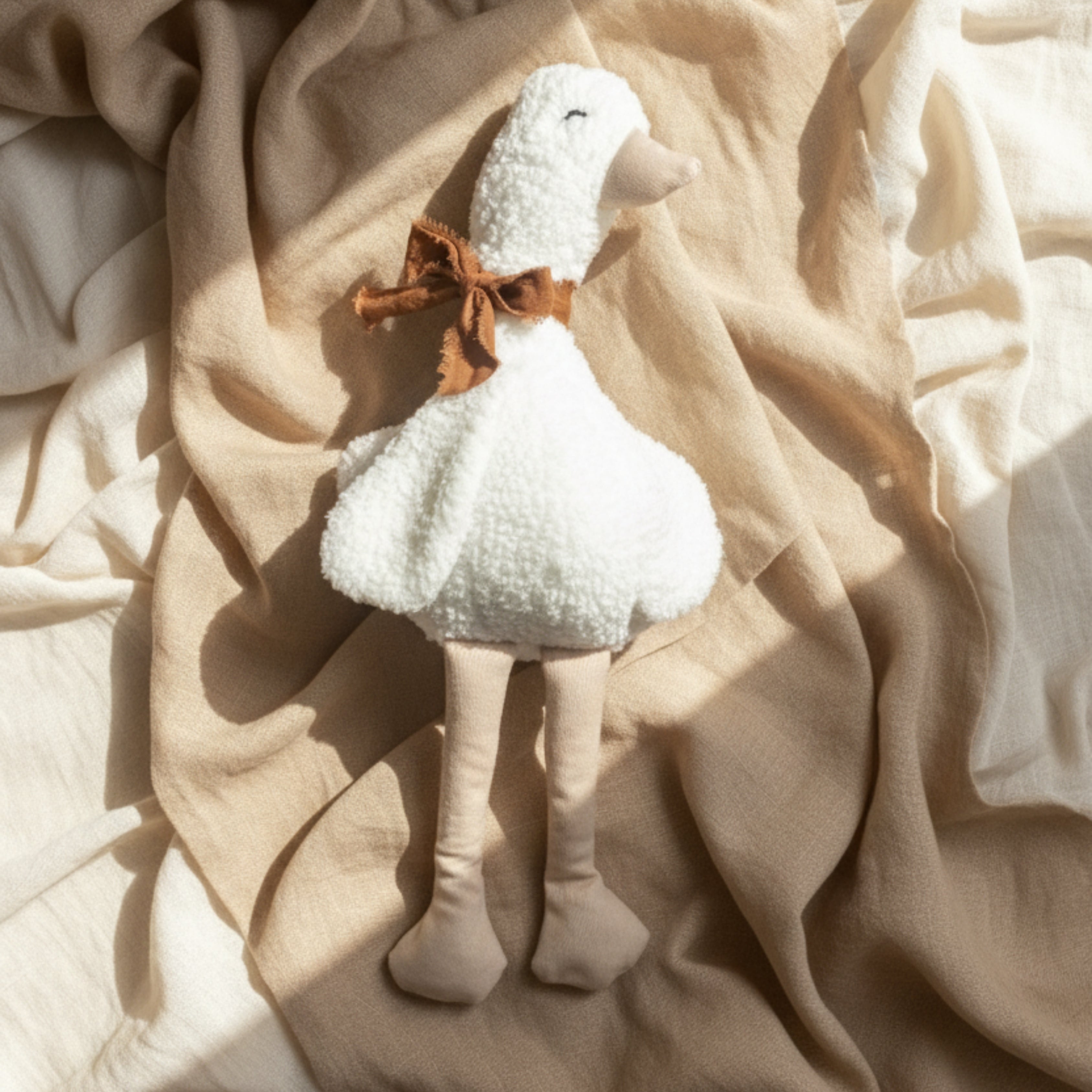 Lenny the Duck Sleep Companion — a handcrafted plush duck with a soft wool texture and a brown bow, resting on beige linen fabric in gentle morning light.